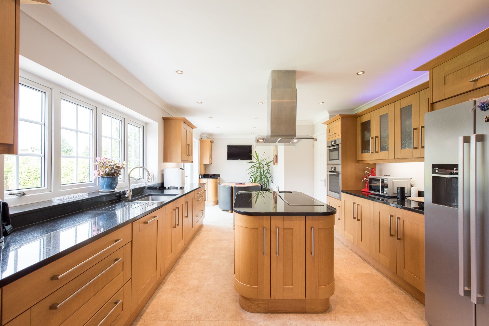 Spacious kitchen with wood cabinets, dark countertops, island, stainless steel appliances, and large windows.