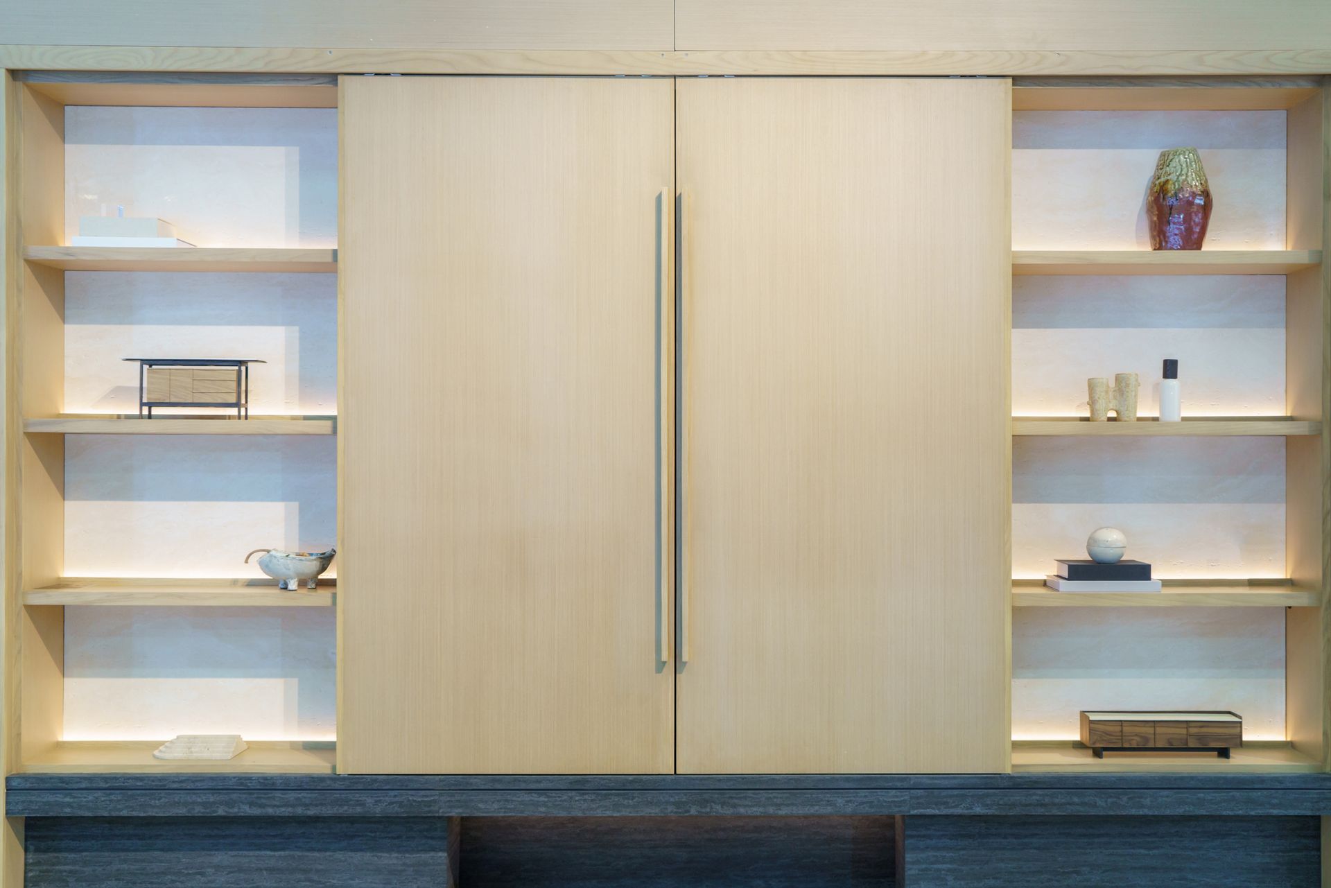 Built-in wooden cabinet with sliding doors flanked by open shelves displaying decorative objects.