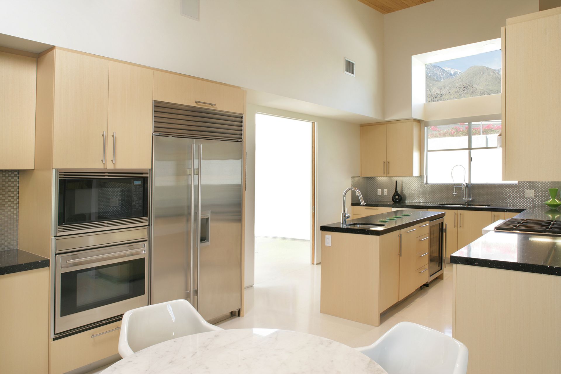 Modern kitchen with stainless steel appliances, light wood cabinets, and black countertops.