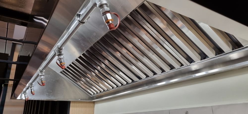 Stainless steel commercial kitchen exhaust hood with vents and sprinkler nozzles on the ceiling