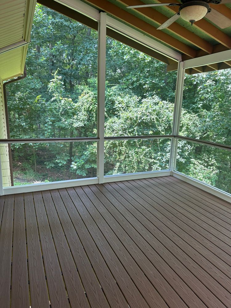 A screened in porch with a wooden deck and a ceiling fan.