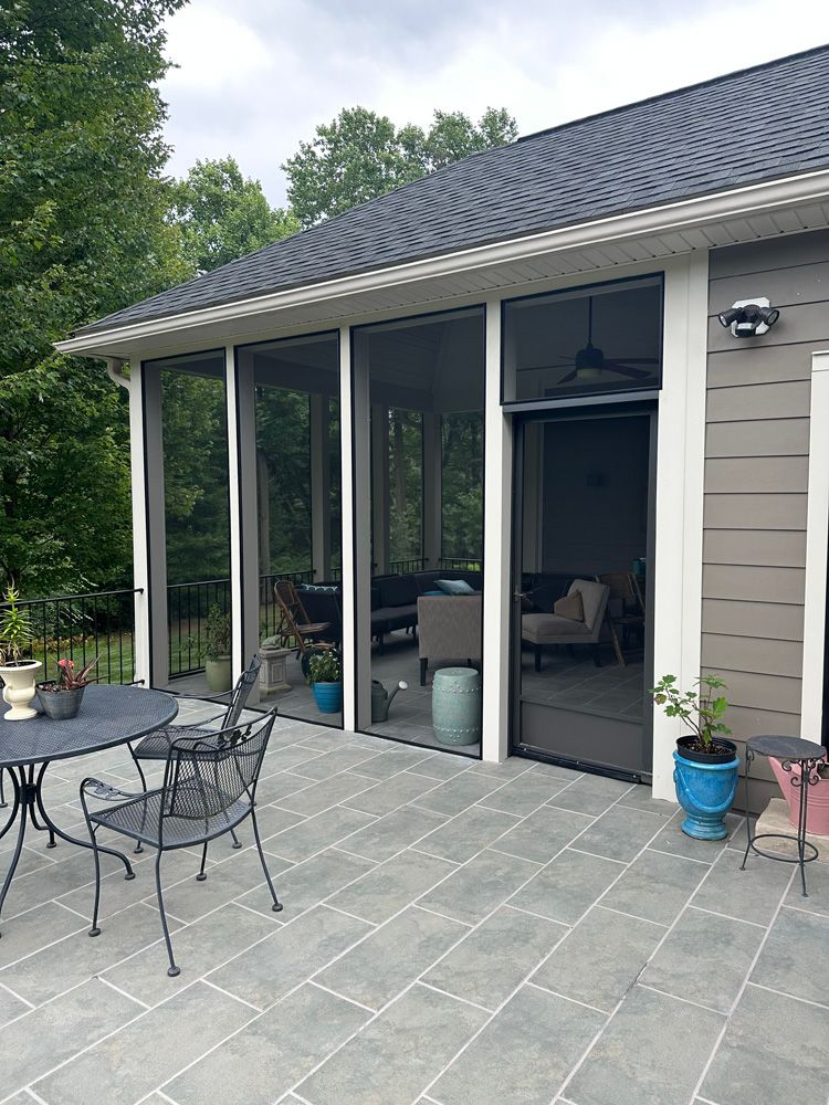A screened in porch with a table and chairs in front of a house.