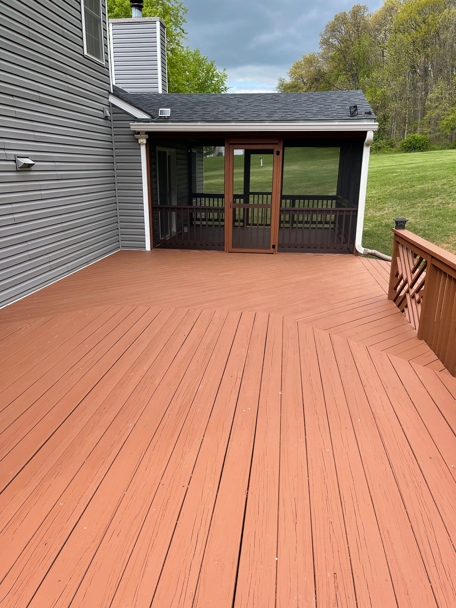 A large wooden deck with a screened in porch next to a house.