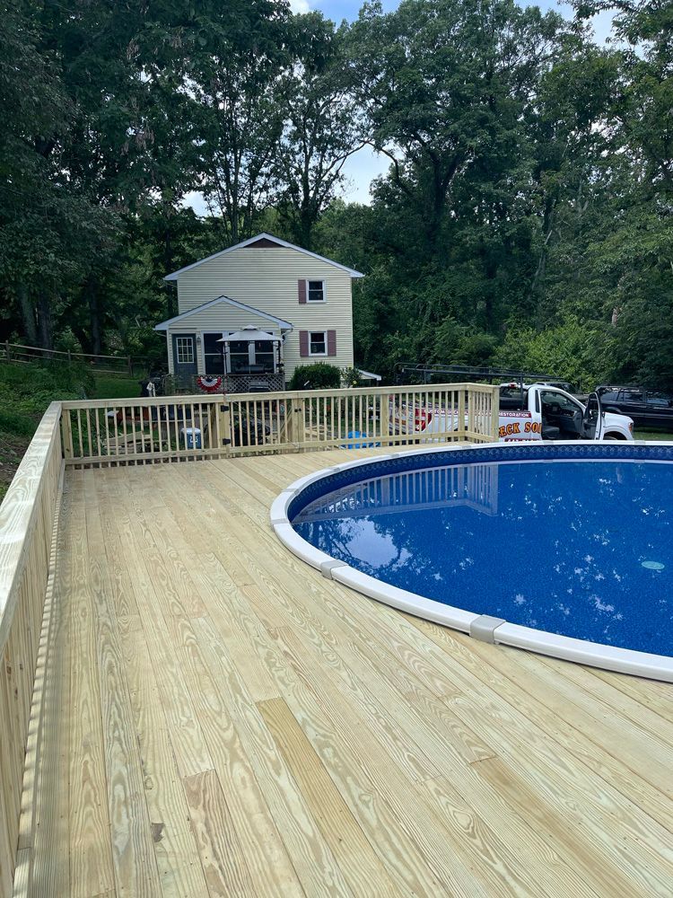 A large swimming pool with a wooden deck in front of a house.