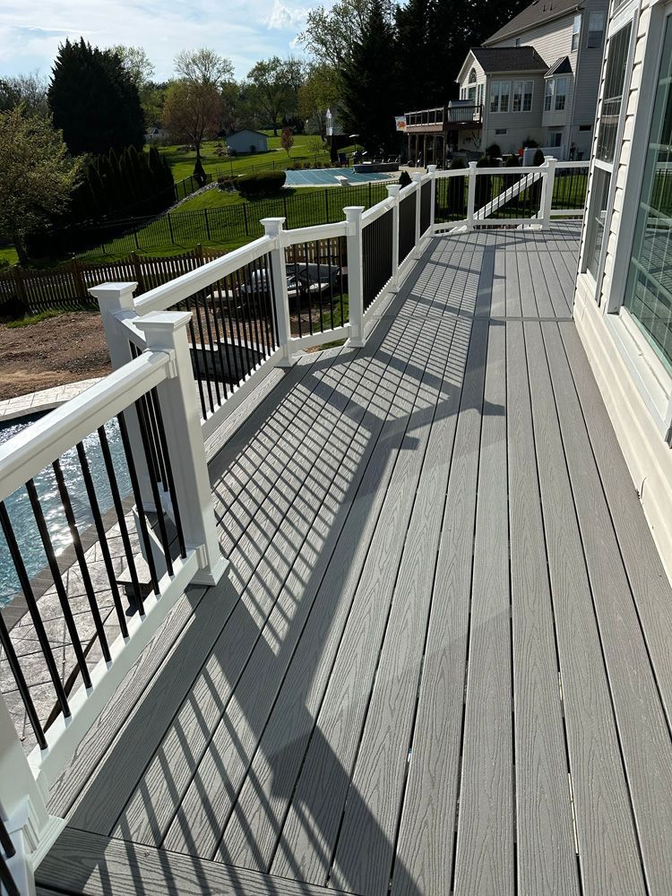 A large deck with a white railing and a pool in the background.