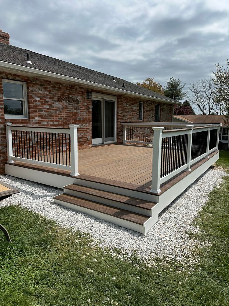 A large deck with a white railing is in front of a brick house.