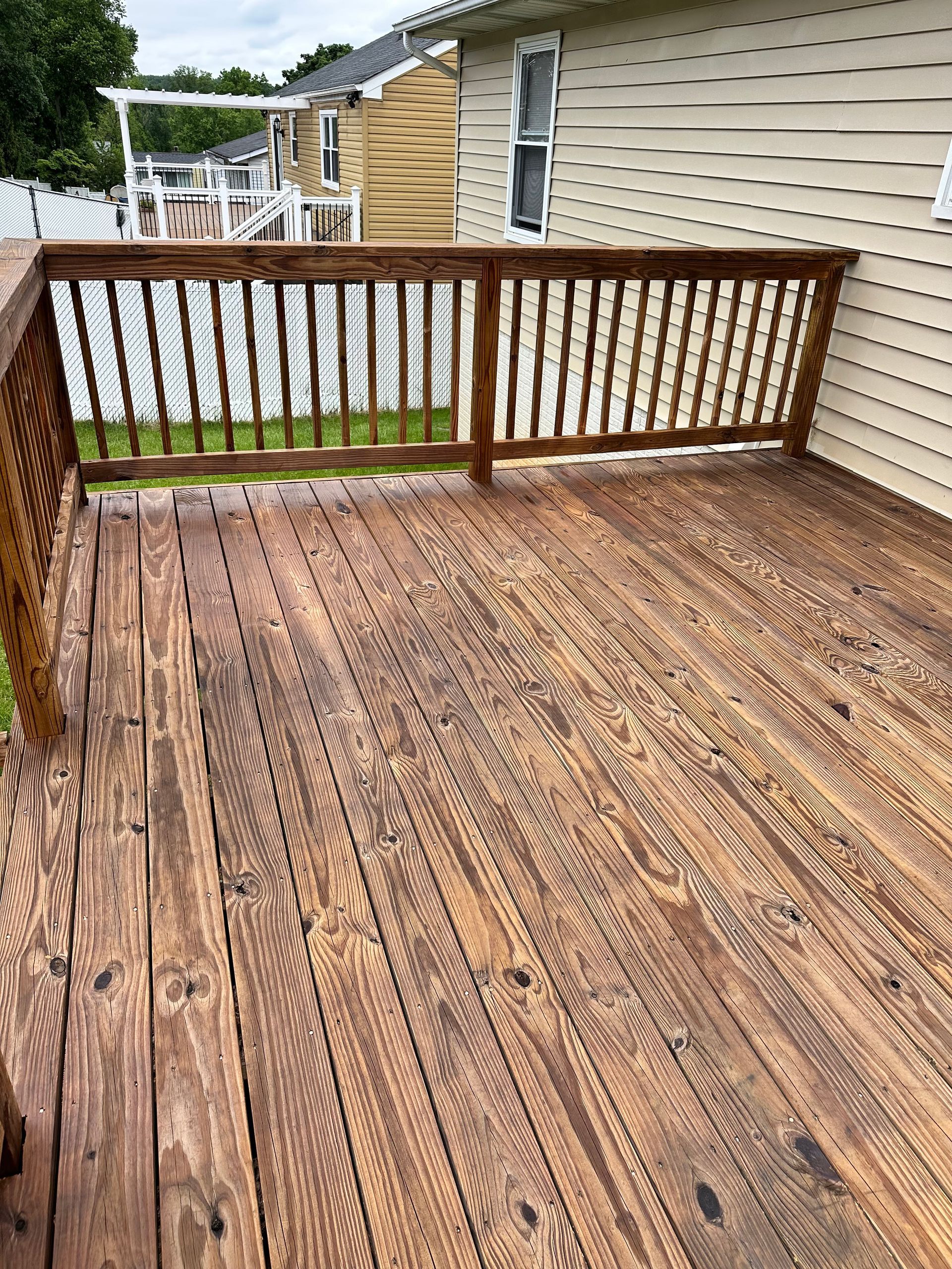 A wooden deck with a railing and a house in the background.