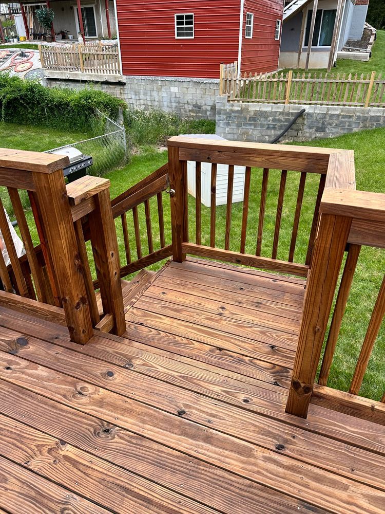 A wooden deck with stairs leading up to it and a red house in the background.