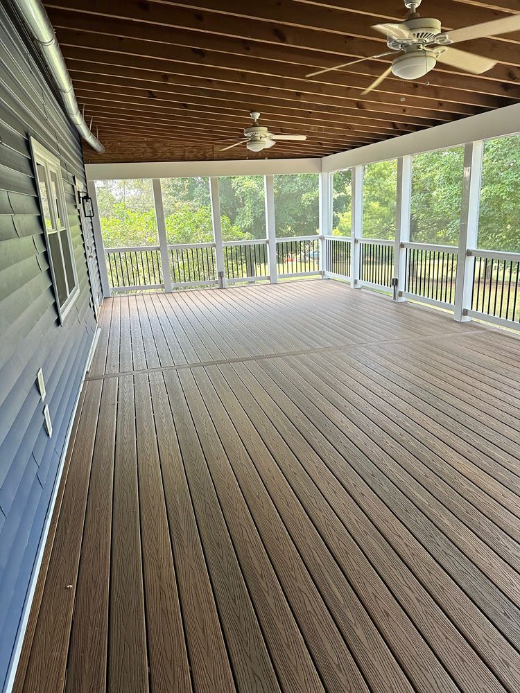 A screened in porch with a wooden deck and ceiling fan.