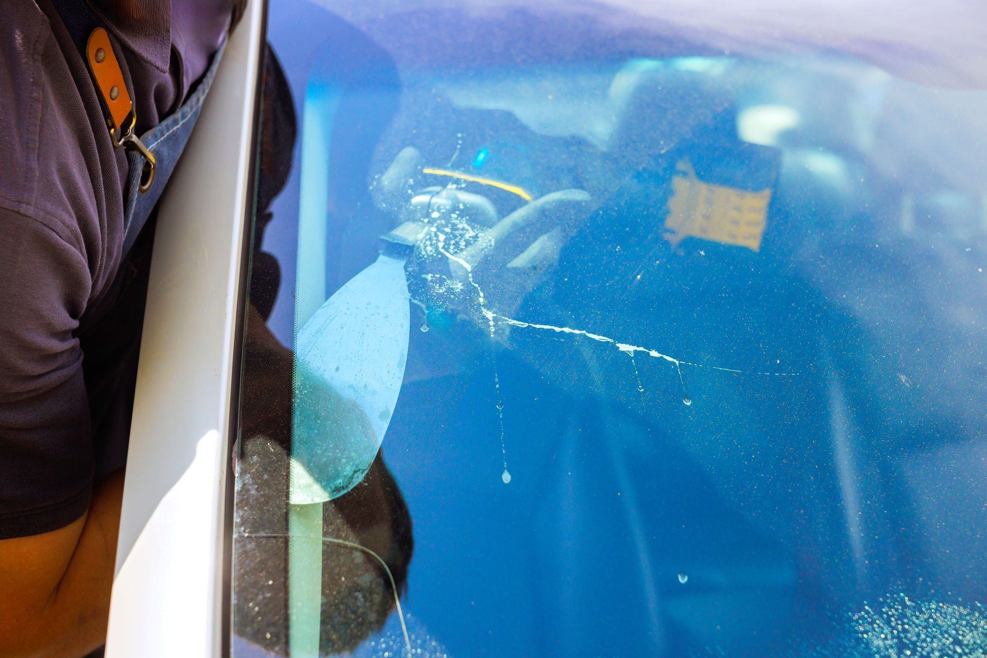 An unrecognized specialist works on replacing a cracked car windshield, using a repair tool.