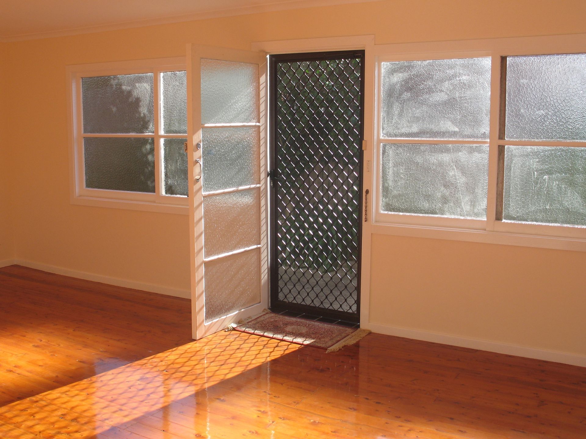 Interior room with open screen door, windows, and hardwood floor bathed in sunlight.
