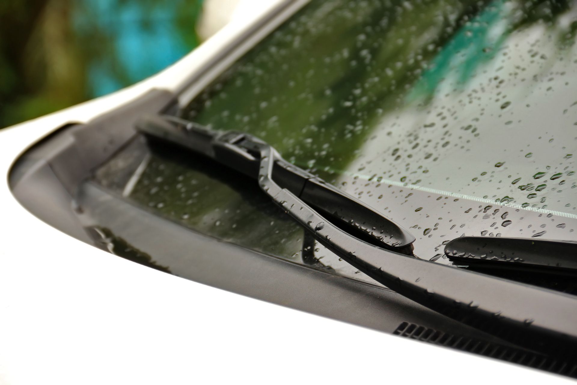 Car windshield with water droplets, black wiper blades, and a white car body.