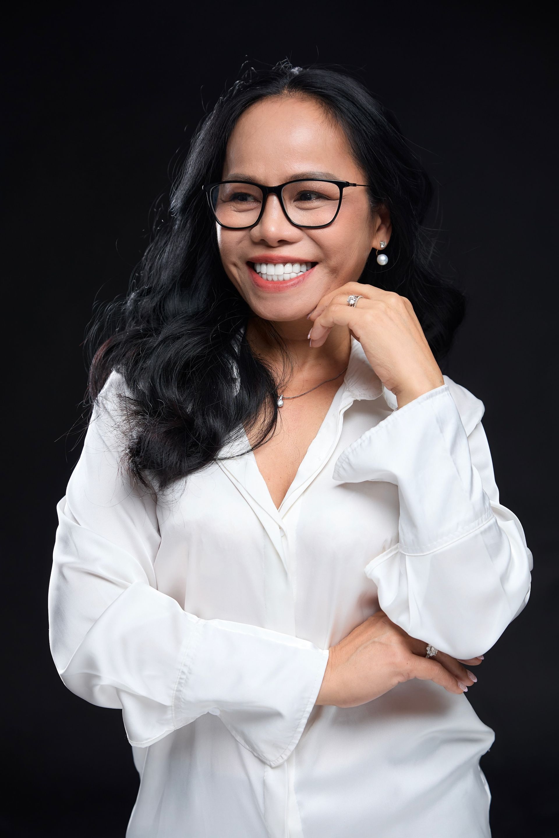 Woman in glasses smiles, wearing a white button-down shirt. Black background.