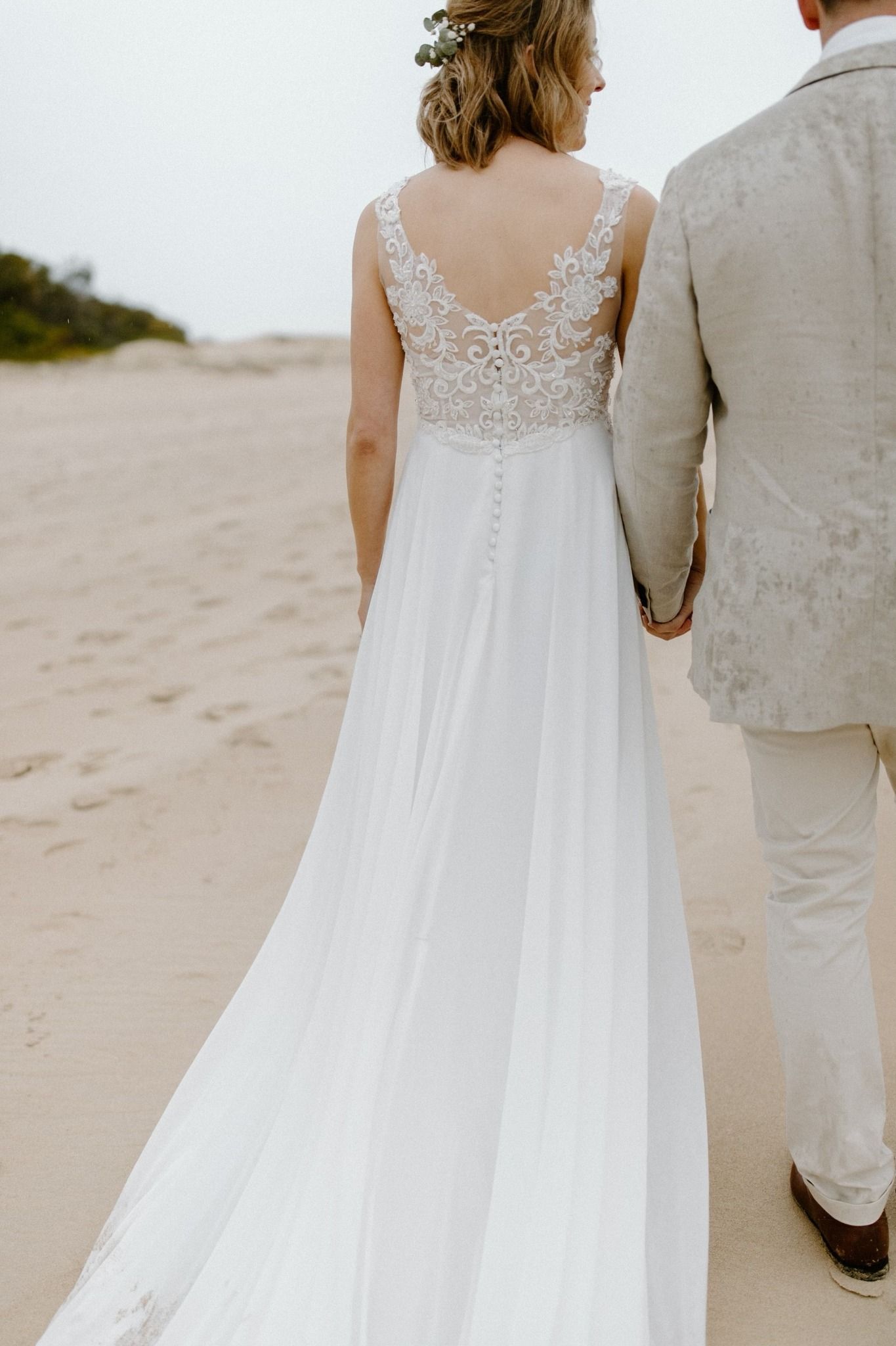 A bride and groom are walking on the beach holding hands.