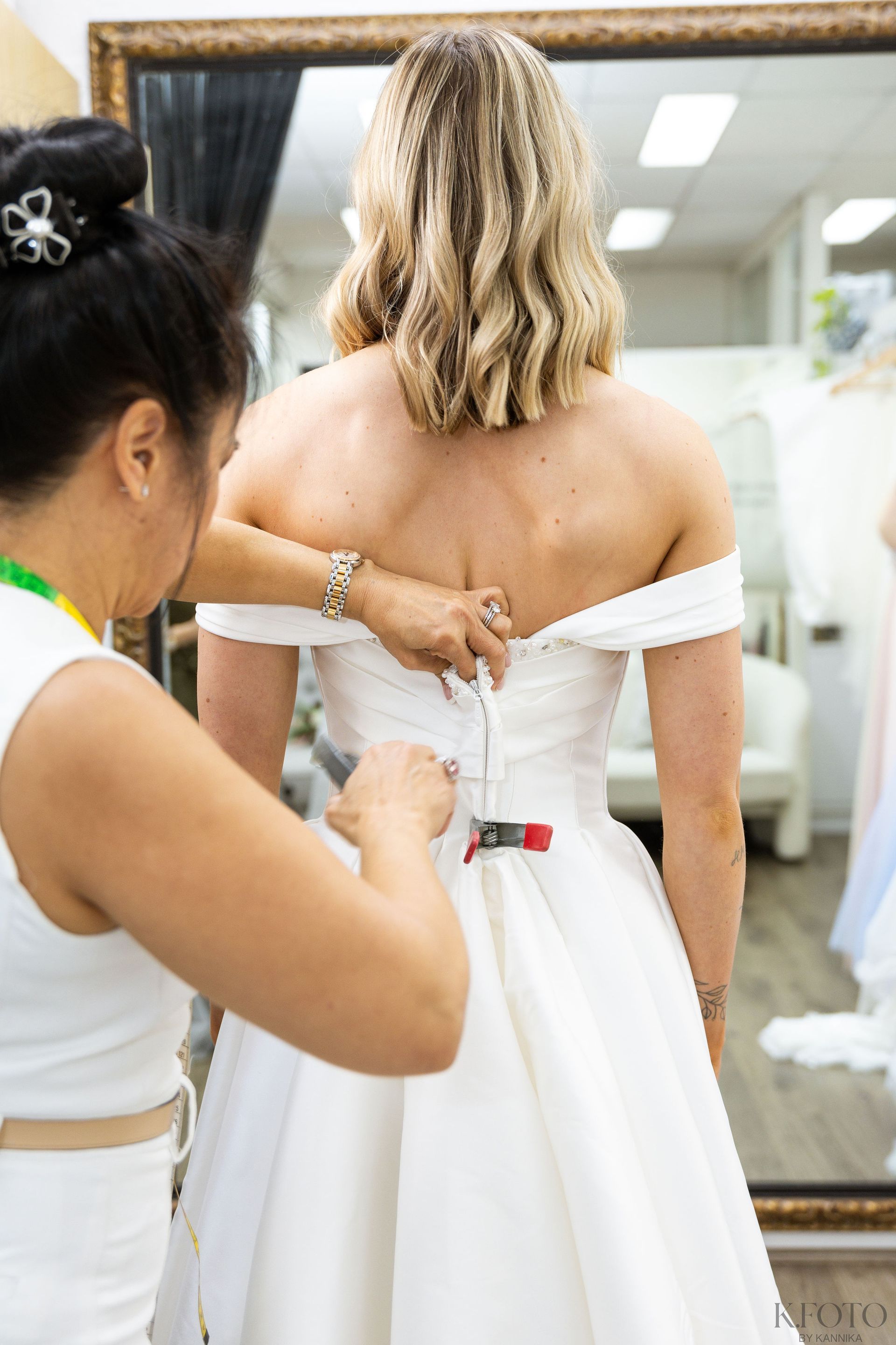 A woman is adjusting a woman 's wedding dress in front of a mirror.