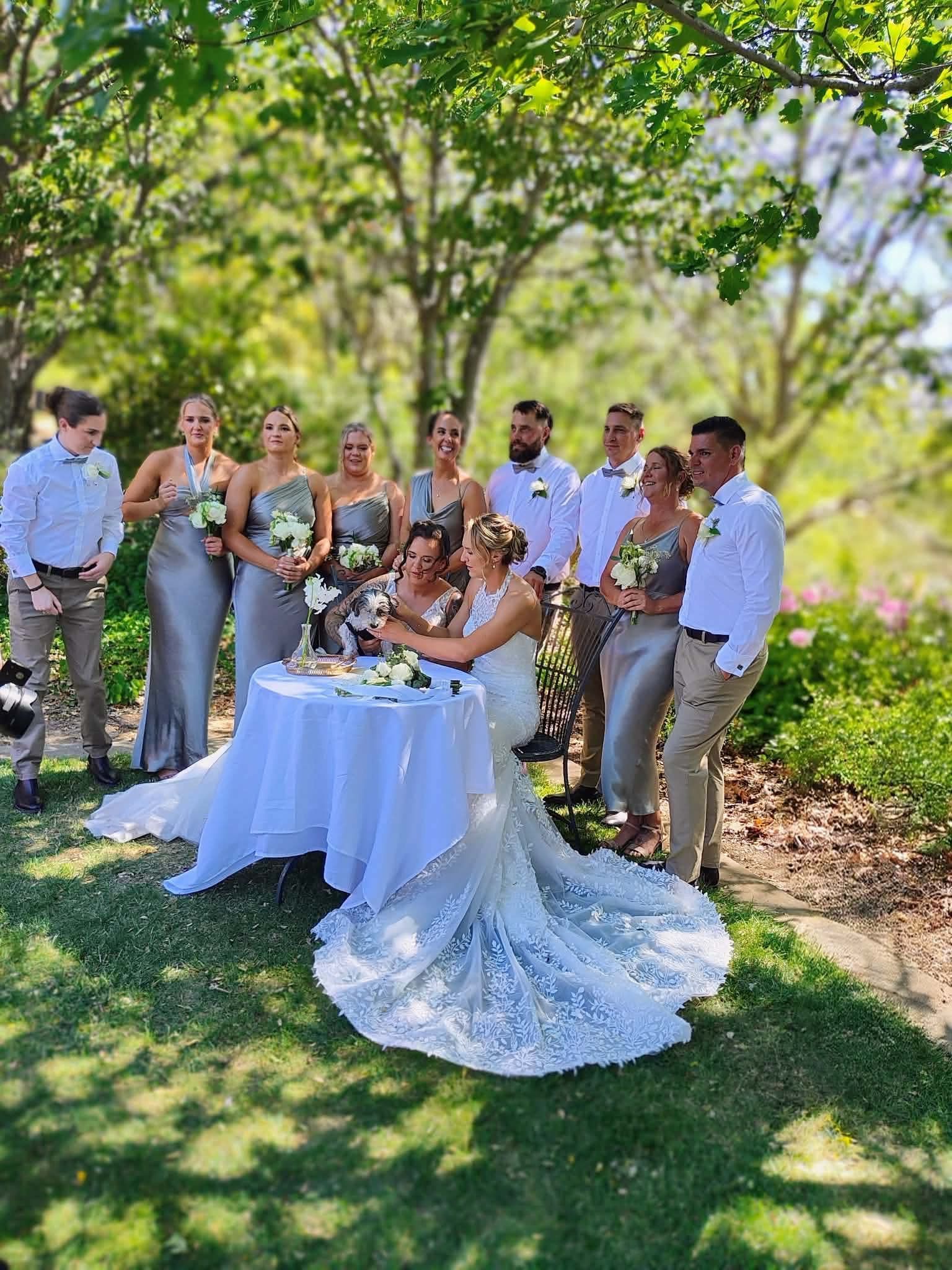 Wedding party signing a document at a table in a garden setting.
