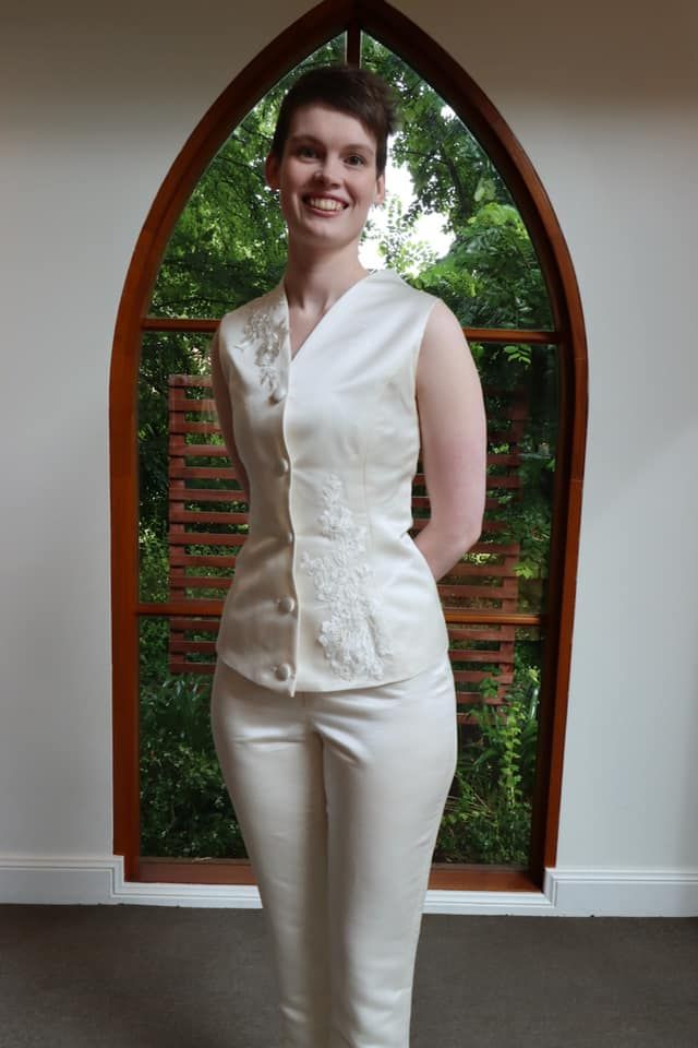 A woman in a white vest and pants is standing in front of a window