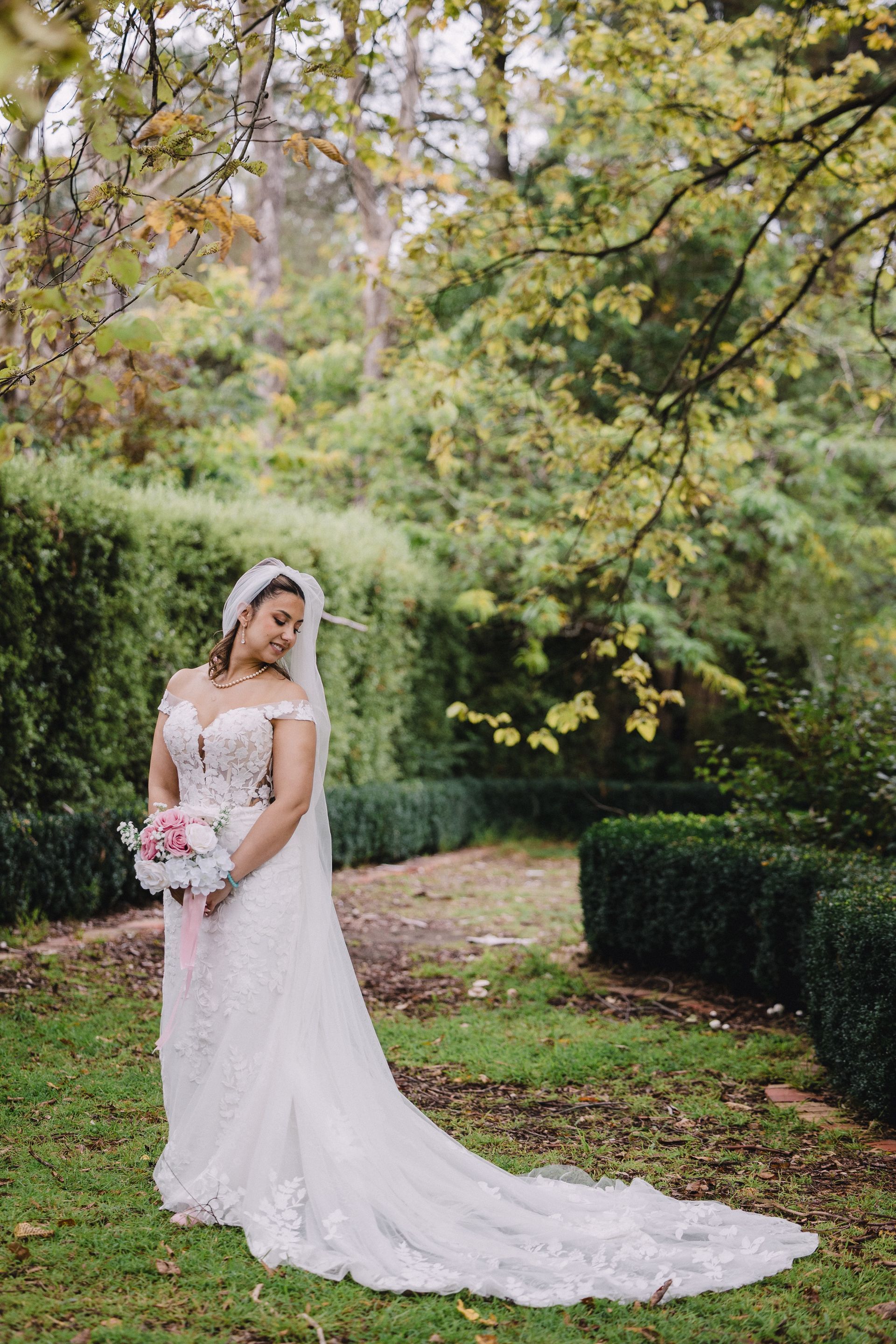 Bride in a white lace gown holding a bouquet in a garden beneath autumn trees