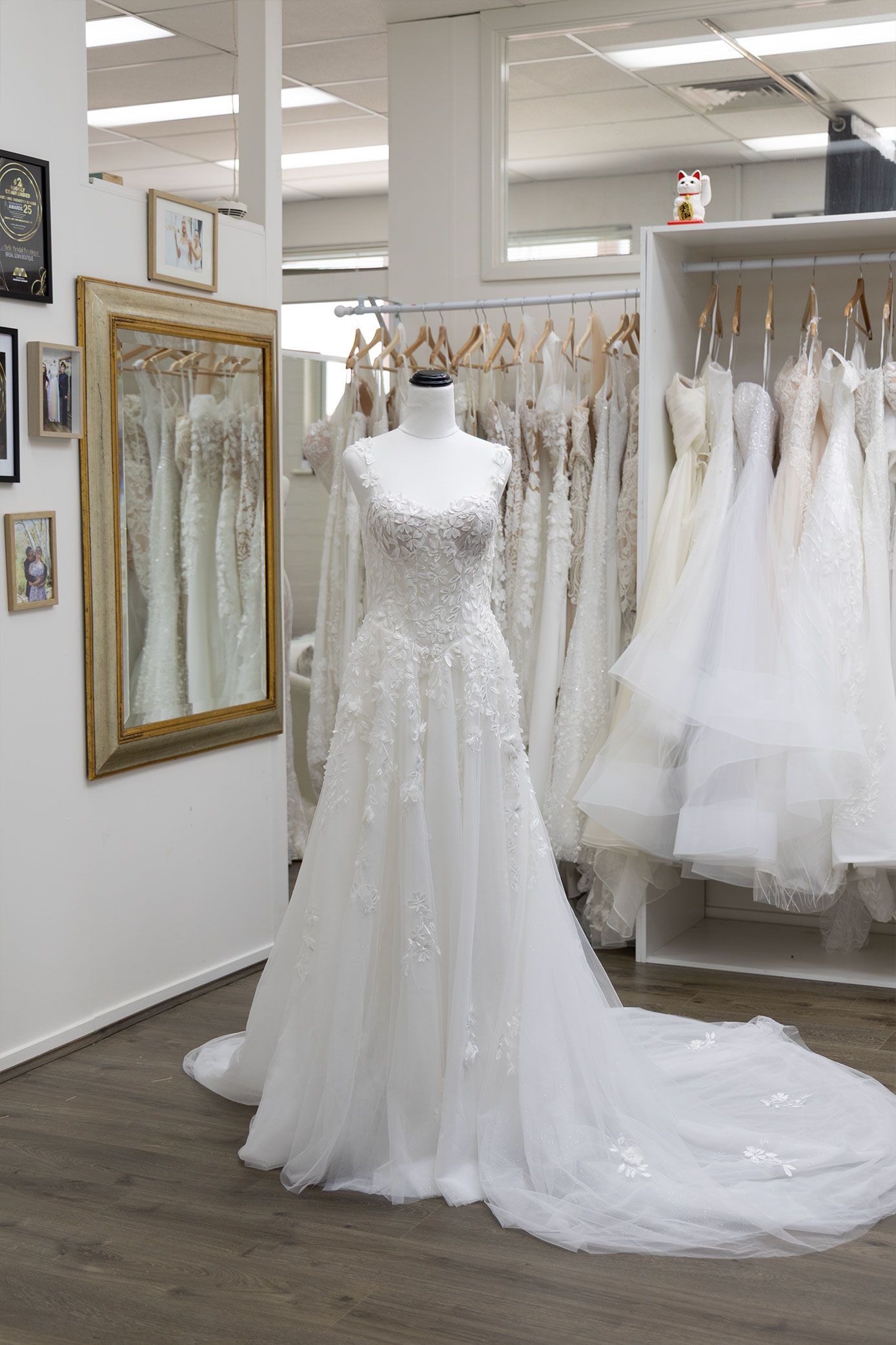 Wedding dress on a mannequin in a bridal shop, with other dresses hanging in the background.