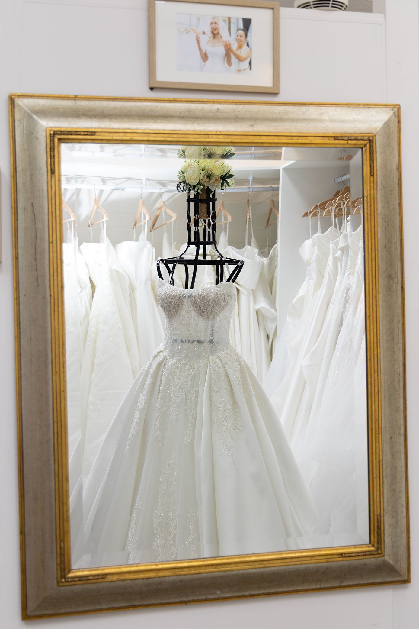 Mirror reflecting a wedding dress on a mannequin in a bridal shop, framed with other dresses.