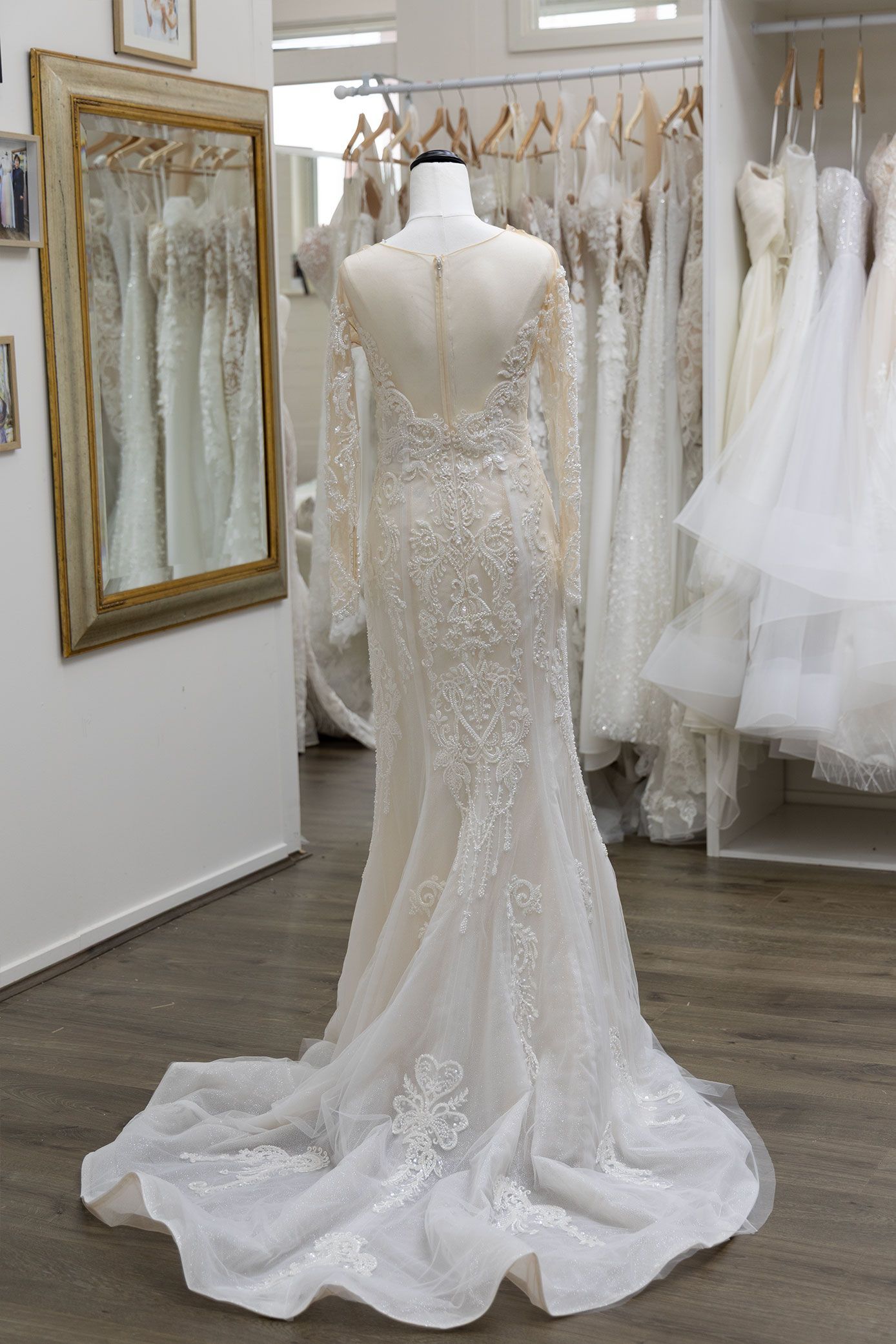 Wedding dress on a mannequin, in a bridal shop. Long sleeves, embellished bodice, train.