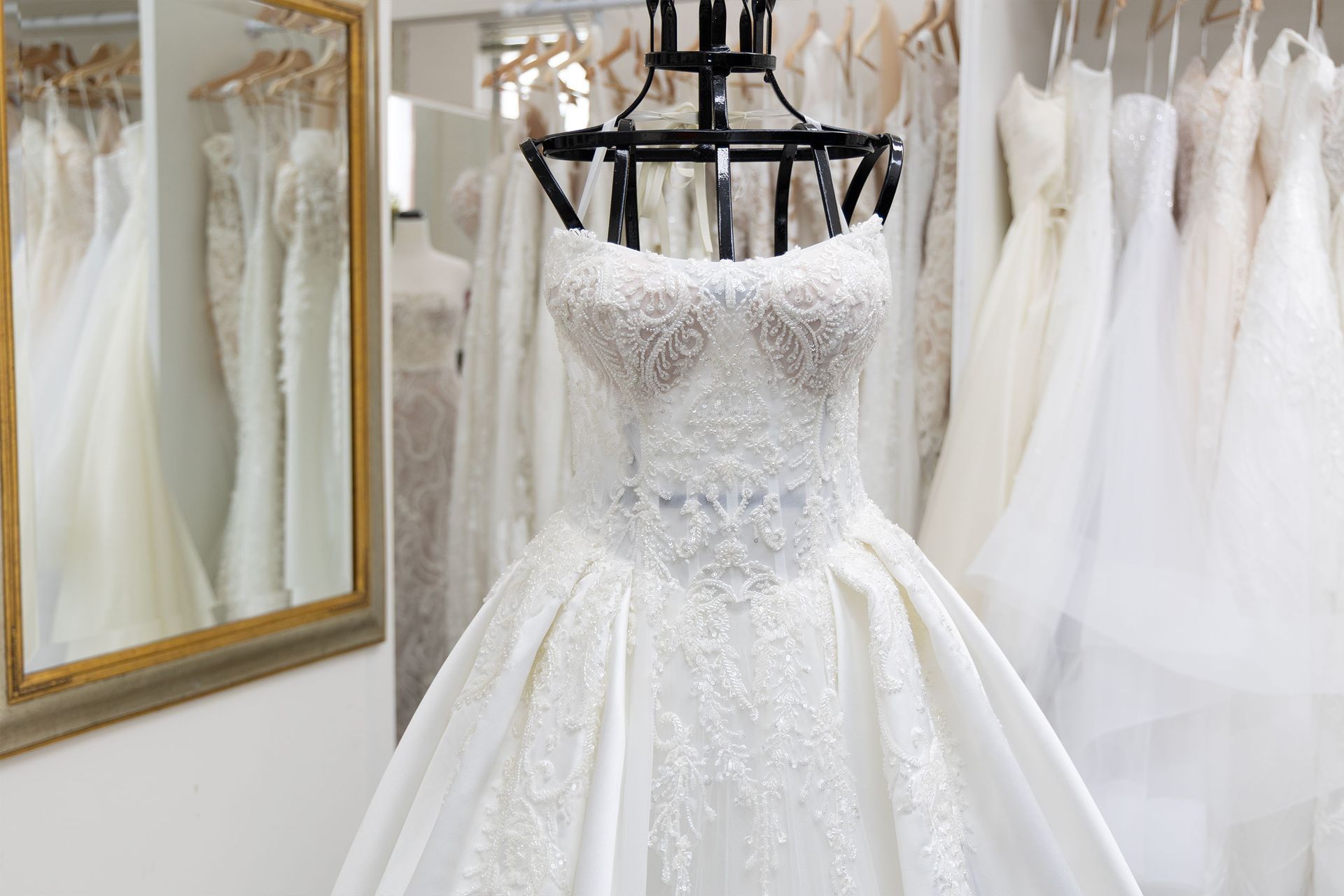 Wedding dress on a mannequin in a bridal shop, surrounded by more dresses, mirrored wall.