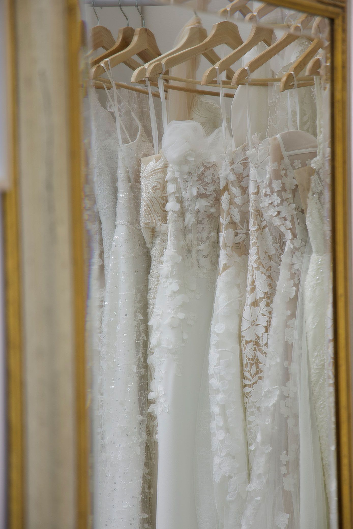 Wedding dresses hanging in a gold-framed mirror, reflecting a clothing boutique.