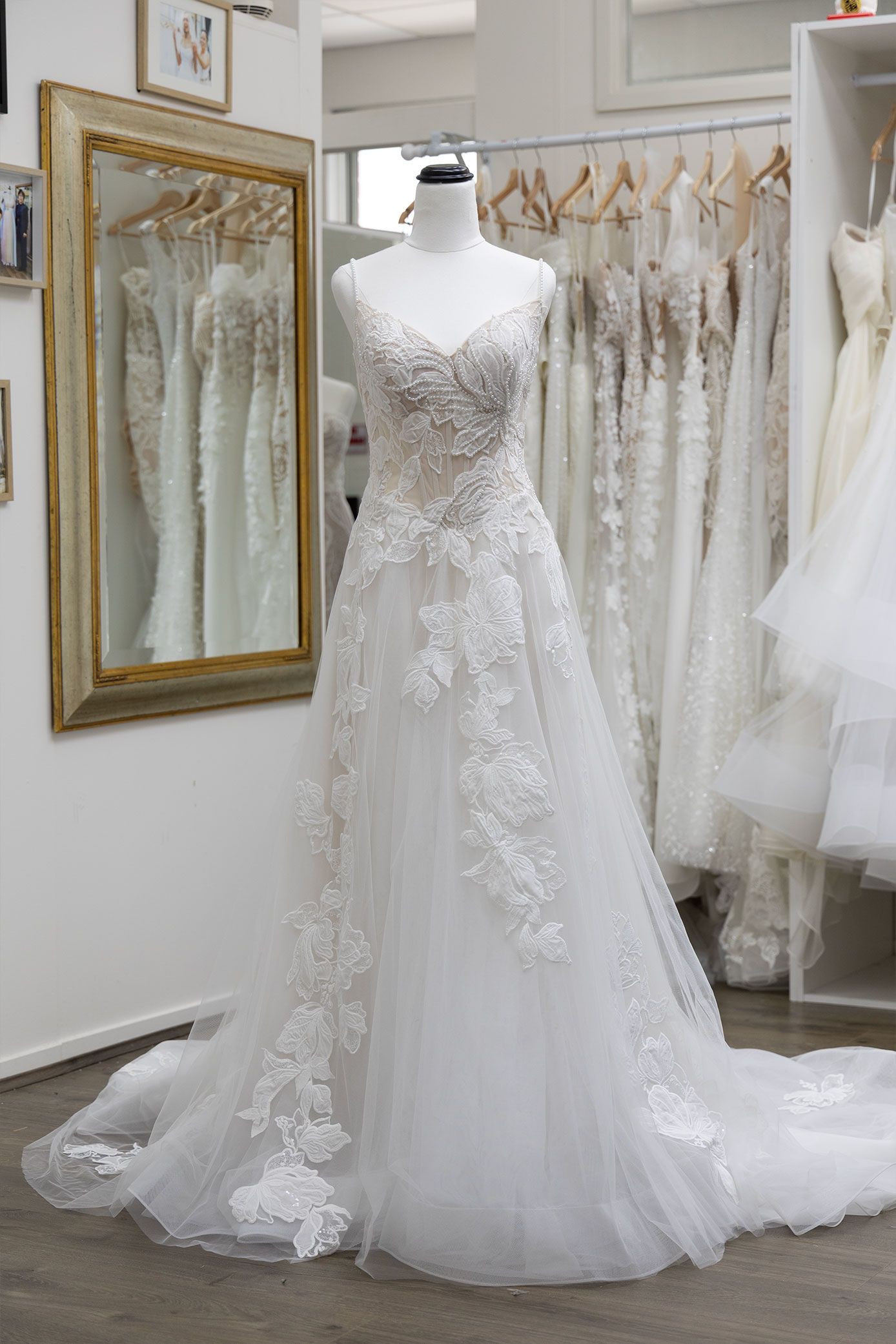 White wedding dress with floral lace on a mannequin in a bridal shop.