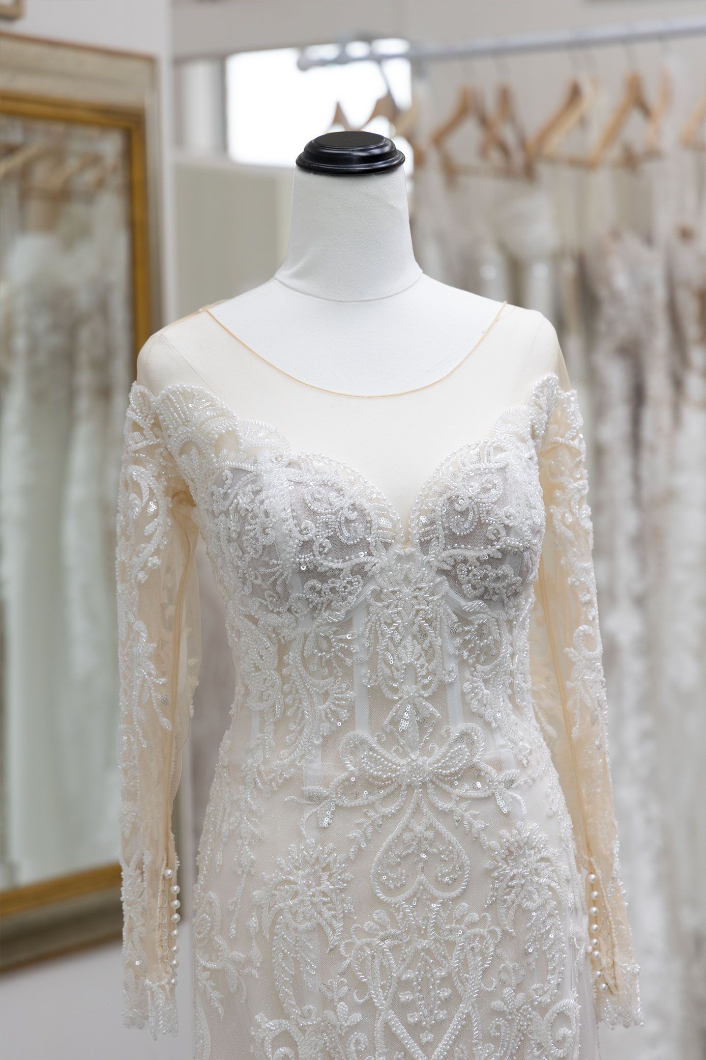 Wedding dress on a mannequin, long sleeves, embellished lace, cream color, in a bridal shop.