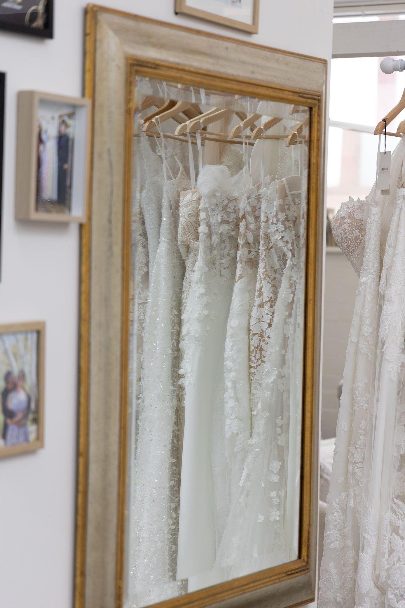Mirror reflecting white wedding dresses hanging in a boutique, gold frame.