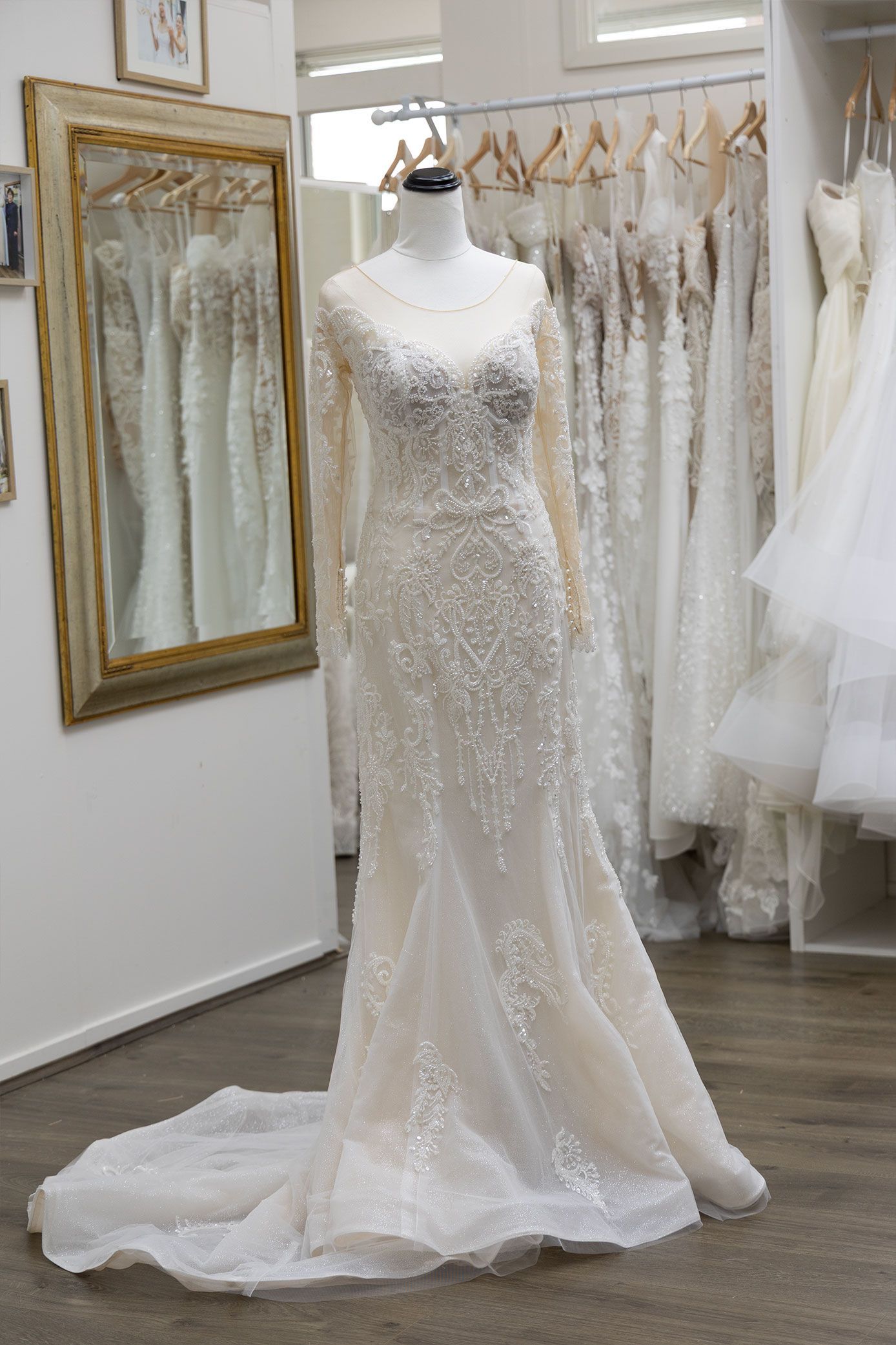 Wedding dress on a mannequin in a bridal shop, long-sleeved with intricate beading and a train.