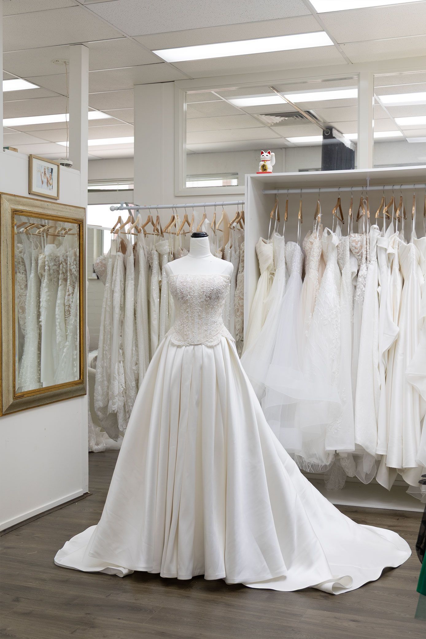 Wedding dress on a mannequin in a bridal shop, surrounded by other white dresses hanging on racks.