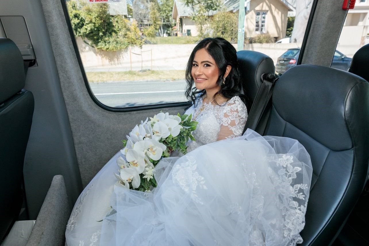 A bride in a wedding dress is sitting in the back seat of a car holding a bouquet of flowers.
