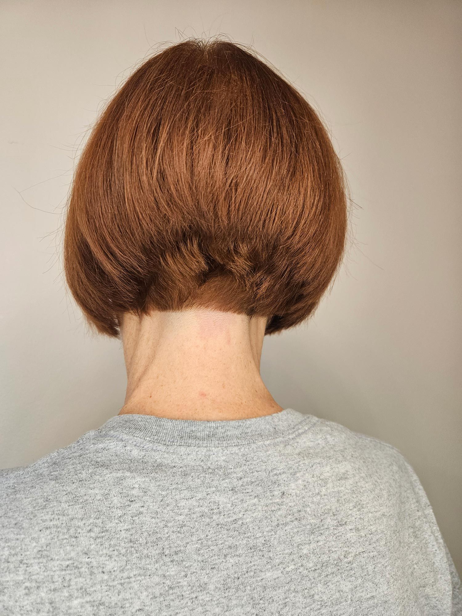 Rear view of a person with a short, reddish-brown bob haircut, wearing a gray sweatshirt.