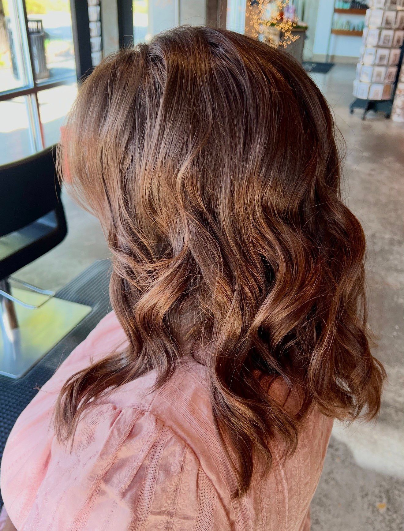 Woman with brown, wavy hair; wearing a pink sweater in a salon setting.