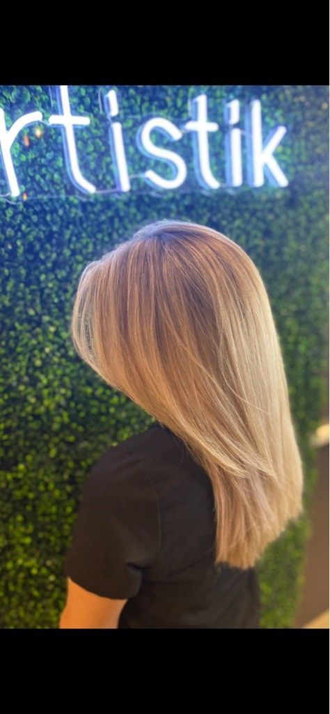 Woman with blonde hair, back to the camera, in front of a green wall with the word “artistik” written in blue neon.