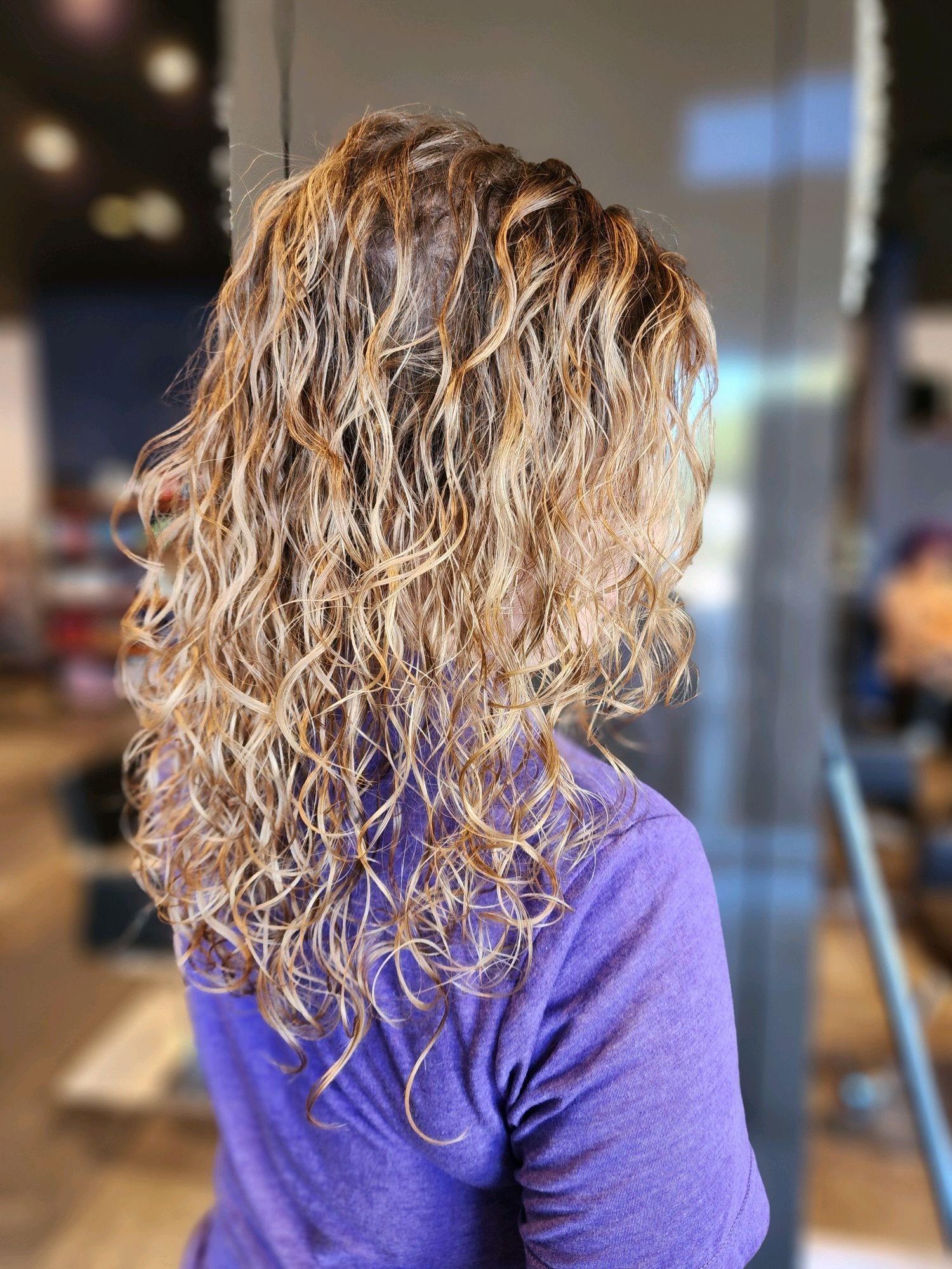 Woman with wavy, light brown hair wearing a purple shirt, indoors.