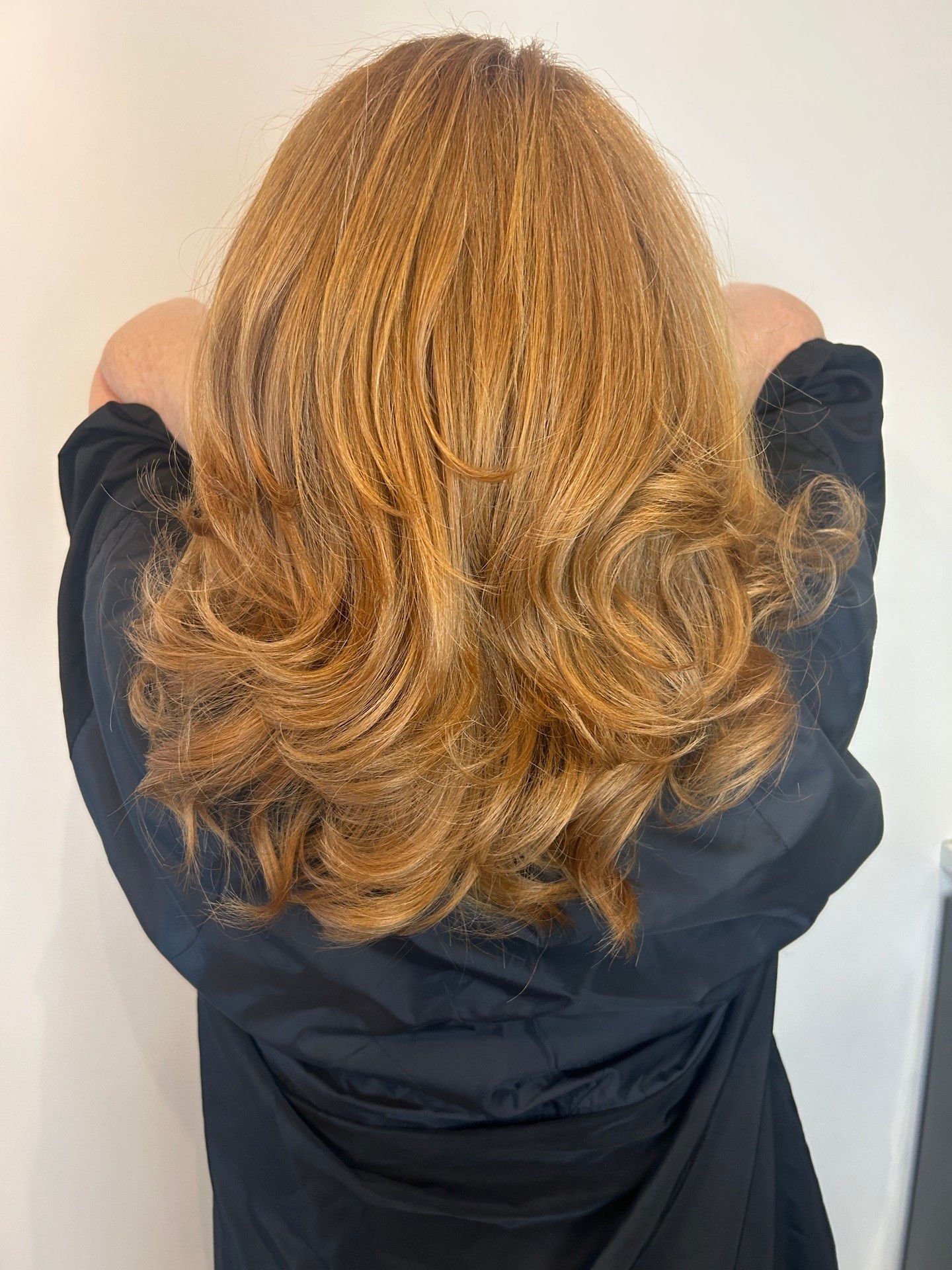 Woman with curled auburn hair, back to the camera, wearing a black garment.