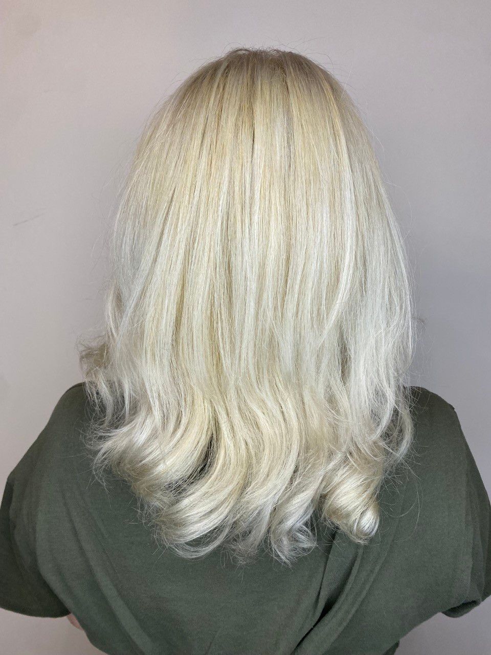Blond, wavy hair styled over a green shirt against a light pink background.