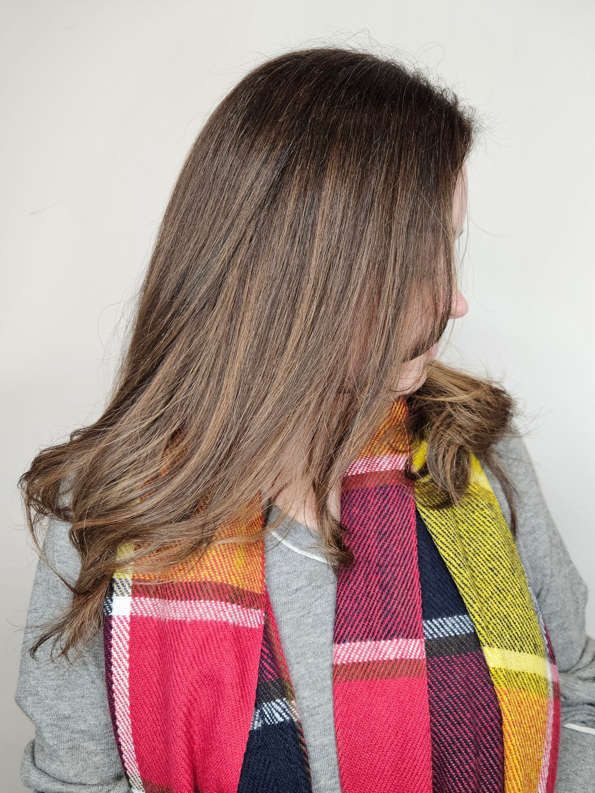 Woman with long brown hair wearing a colorful plaid scarf over a gray shirt, looking to the side.