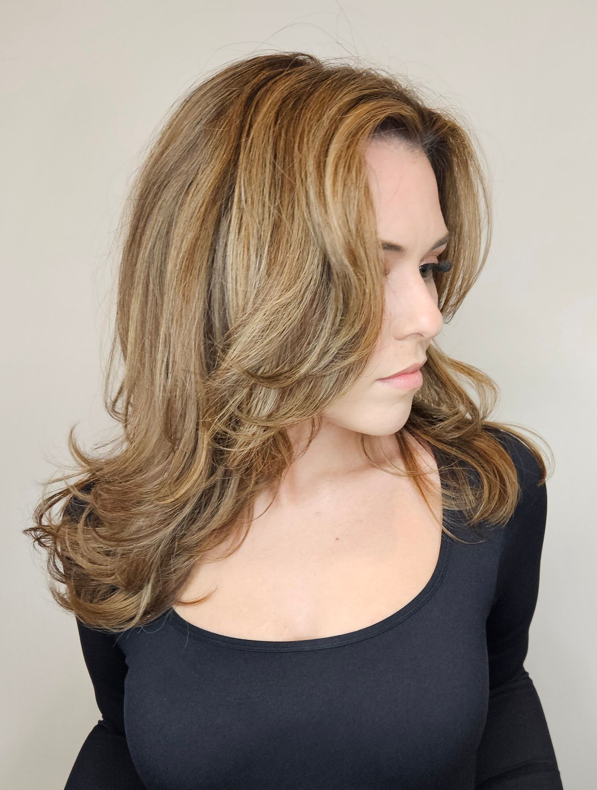 Woman with layered, wavy brown and blonde hair, wearing a black top, looking to the side.