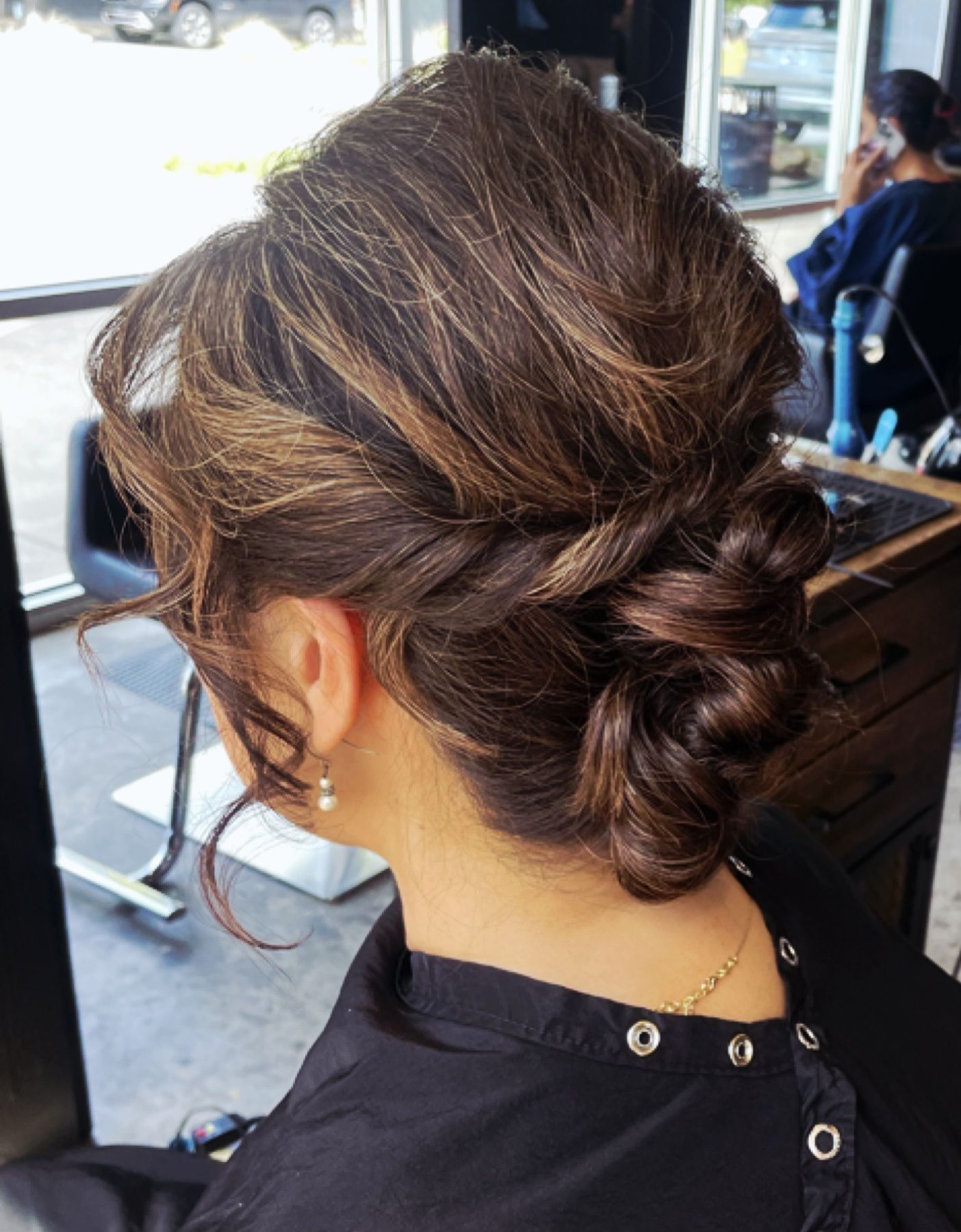 Woman with dark hair in an updo at a salon, brown highlights, side view.