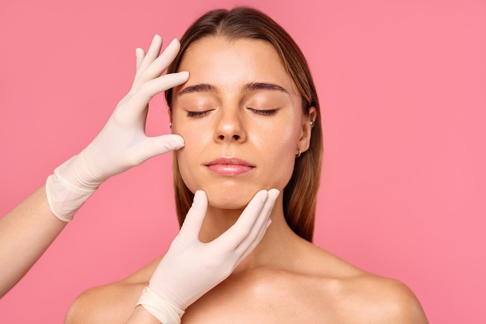 Hands in gloves examining a woman's face, eyes closed — Embrace Cosmetic Clinic in Bundaberg North, QLD