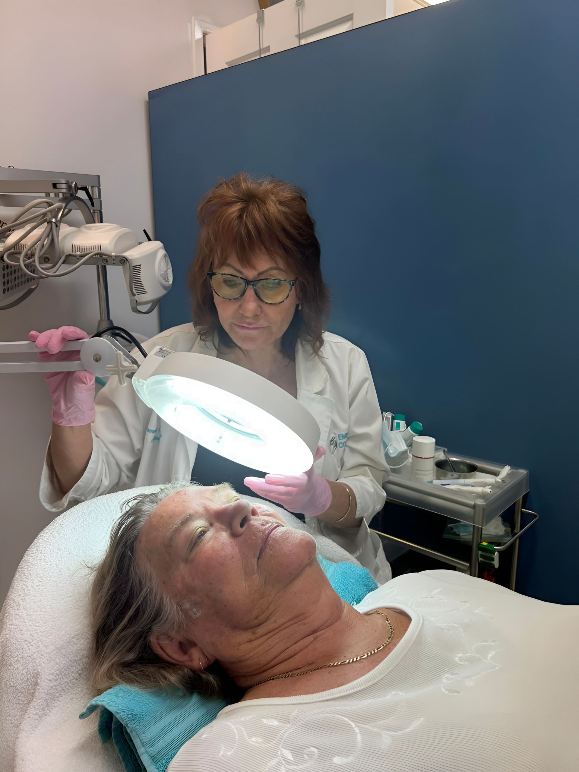 Woman Receiving Facial Treatment Under Bright Magnifying Lamp — Embrace Cosmetic Clinic in Bundaberg North, QLD