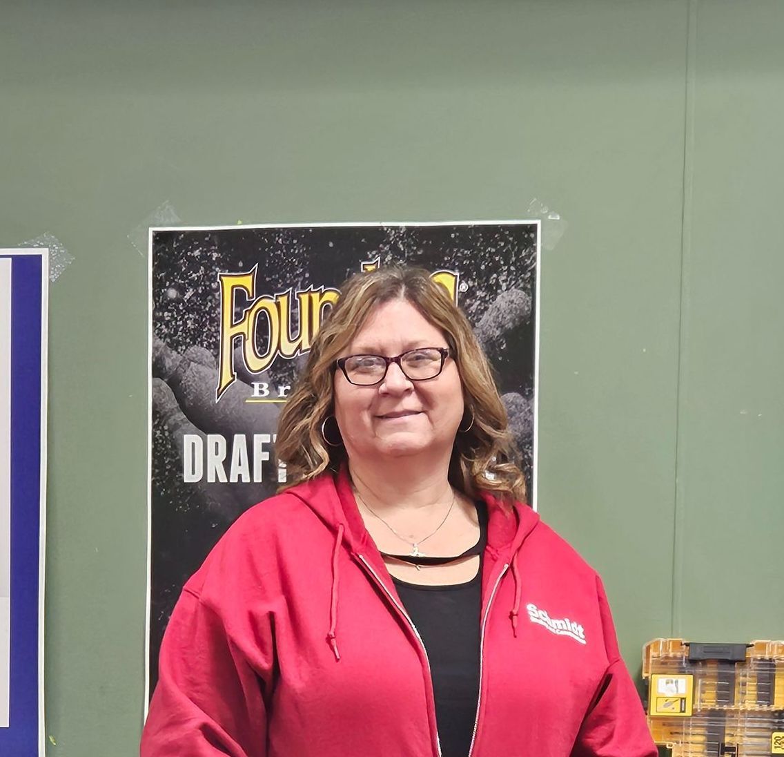 Woman in red hoodie smiles in front of a draft beer advertisement.