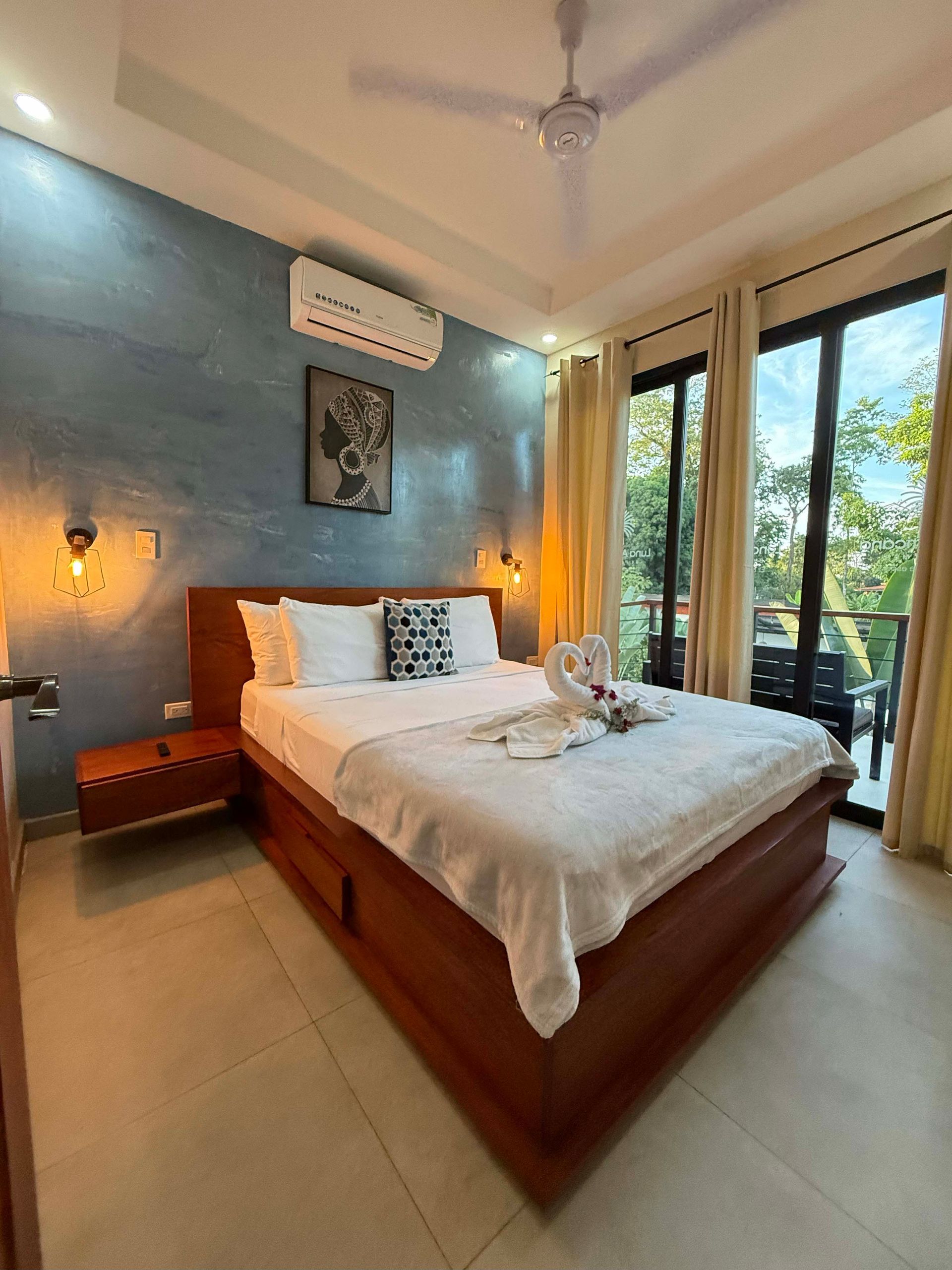 Bedroom with a bed, nightstand, and large windows. The walls are blue, and the bed has white linens.