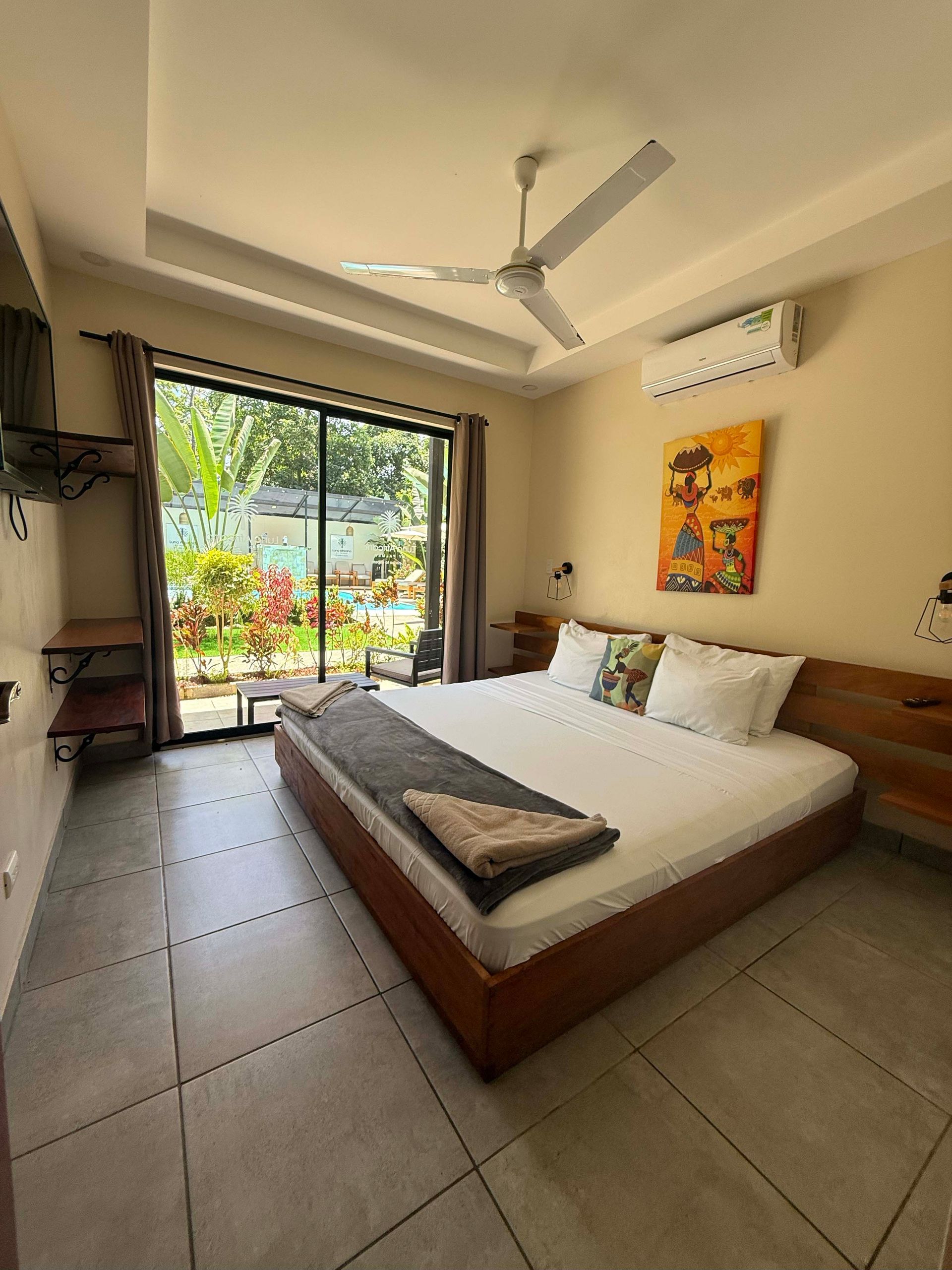 Bedroom with large bed, sliding glass doors to a garden, and artwork on the wall.
