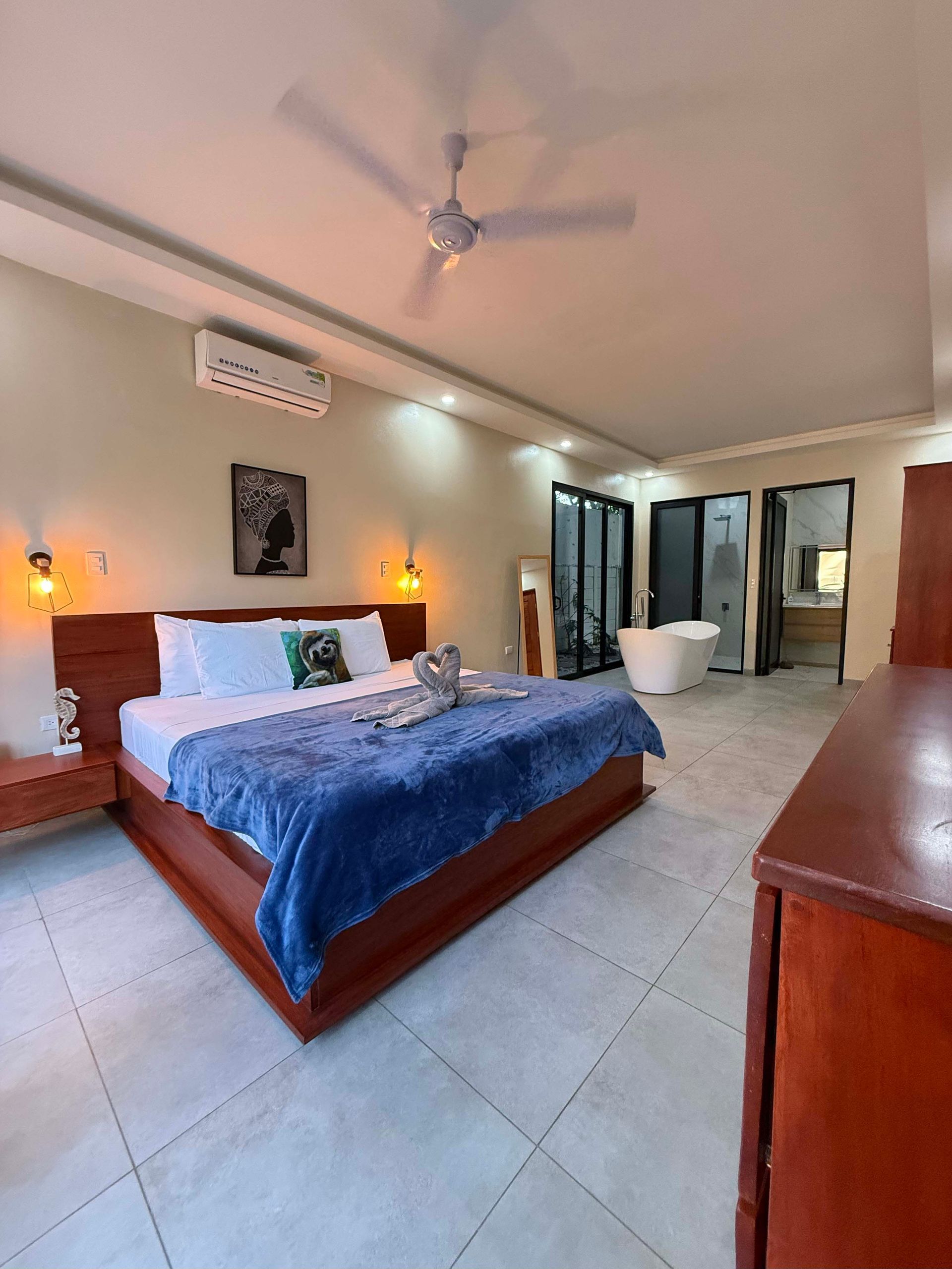 Spacious bedroom with a king bed, blue blanket, and en suite bathroom with a soaking tub.