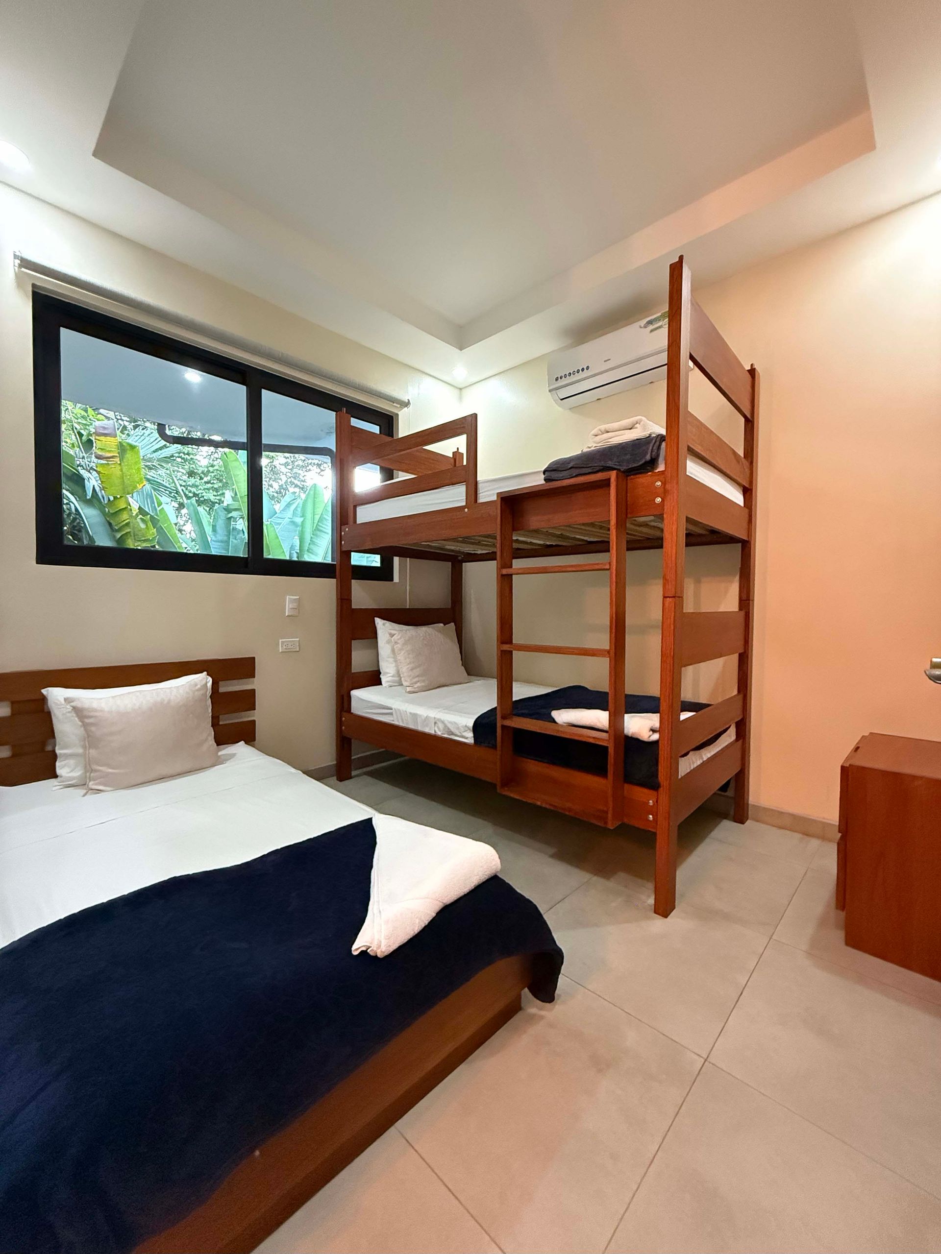 Bedroom with two bunk beds and a twin bed; pale orange walls and a window overlooking greenery.
