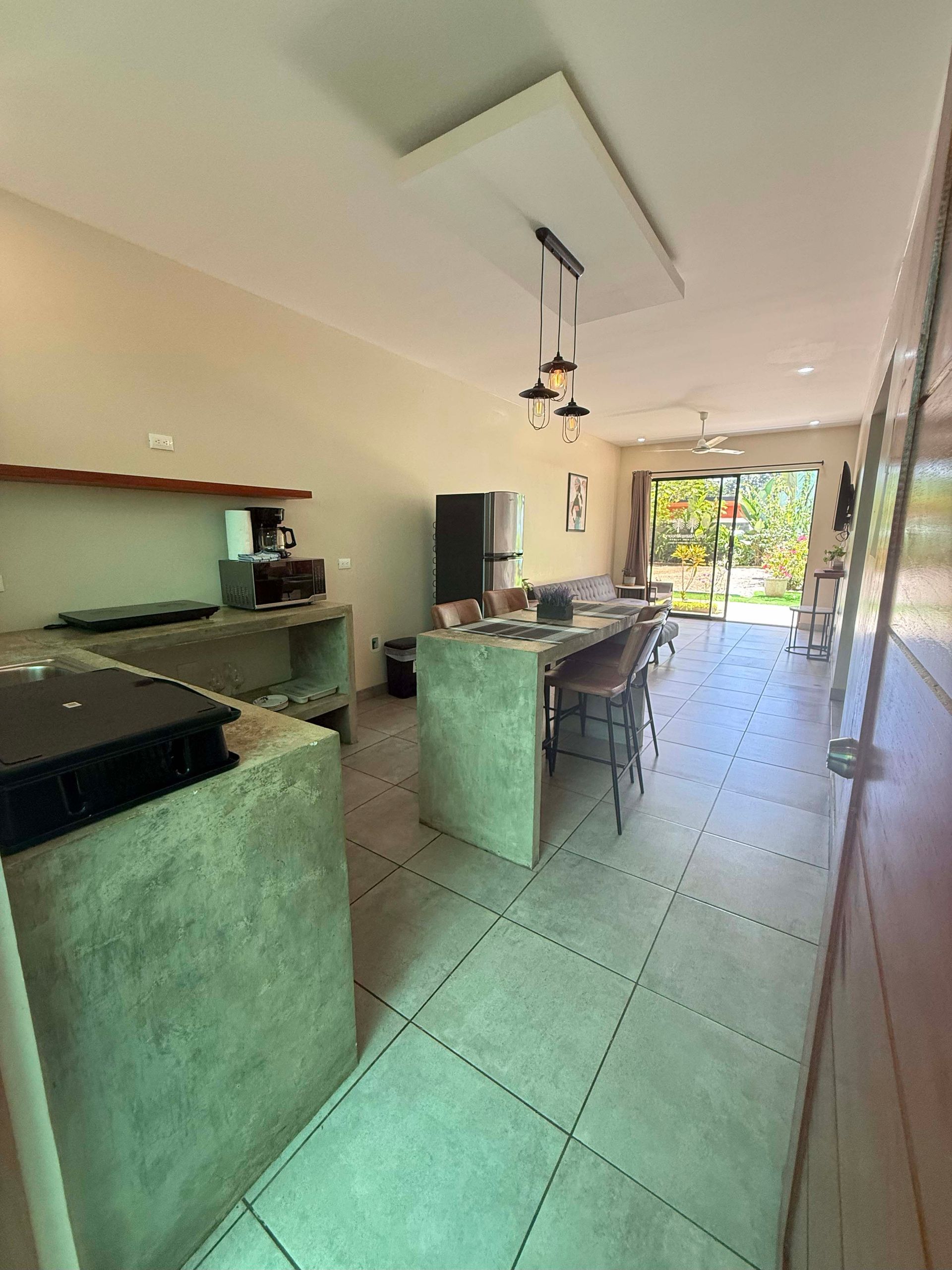 Kitchen with concrete island, black fridge, and dining area leading to outdoor view.